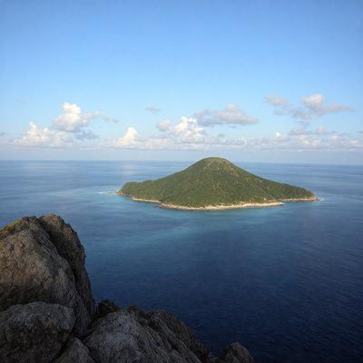 The primary subject of the image is a small island in the middle of a large body of water. The island is surrounded by a vast expanse of water, and it appears to be a lone island in the middle of the ocean. The setting is a serene and peaceful environment, with the island being the main focus of the image. The visual style is a realistic representation of the island and its surroundings. The colors and mood of the image are predominantly blue, which adds to the calm and serene atmosphere of the scene.